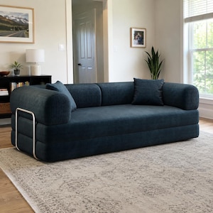 May include: A dark blue corduroy sofa featuring a low-profile design with rounded armrests and a silver-toned metal frame accent on the side. The sofa includes two matching square throw pillows and has a textured, ribbed fabric finish throughout.