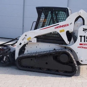 Könnte beinhalten: Ein weiß-schwarzer Bobcat T190 Kompakt-Kettenlader mit rotem Akzent. Der Lader hat eine schwarze Kabine mit Schutzgitter und schwarze Ketten. Der Arm trägt den Text "PACZYNSCY.pl" in Rot.