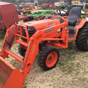 May include: An orange Kubota tractor with a front-end loader. The tractor has large, black tyres and a black seat. The Kubota logo is visible on the bonnet. The tractor is parked on a grassy area.