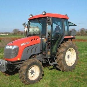 Puede incluir: Un tractor rojo y gris con cabina de cristal, estacionado en un campo cubierto de hierba bajo un cielo azul claro. El tractor tiene neumáticos grandes y un parachoques delantero. El nombre del modelo del tractor es visible en el lateral.