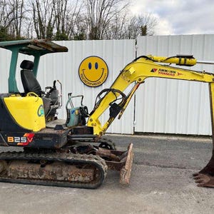 Peut inclure: Une mini-pelle Yanmar B25V jaune et noire avec un auvent vert. L'excavatrice a un siège et des chenilles noirs. Le godet est marron. L'image montre également un panneau smiley.