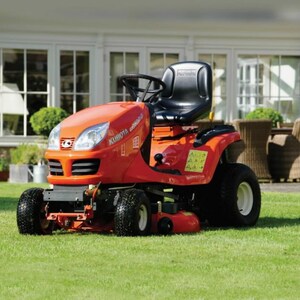 Könnte beinhalten: Ein orangefarbener Kubota Aufsitzmäher mit schwarzem Sitz und Lenkrad steht auf einem grünen Rasen. Der Mäher hat schwarze Reifen und weiße Felgen. Im Hintergrund ein Haus mit weißen Fenstern und eine Terrasse.