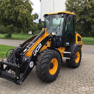 Può includere: Un caricatore gommato JCB 409 giallo e nero con pneumatici di grandi dimensioni. Il caricatore ha una cabina con finestre e un attacco a benna frontale. Il numero 20 è visibile sulla parte anteriore. La macchina è parcheggiata su una superficie pavimentata.