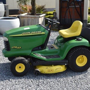 Puede incluir: Cortacésped con asiento John Deere LTR155 verde con asiento y ruedas amarillas. El cortacésped tiene neumáticos negros y una plataforma de corte amarilla. El logotipo de John Deere es visible en el capó.