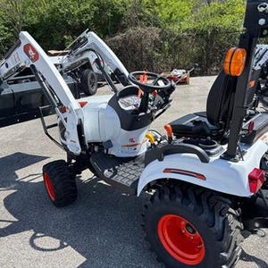 May include: A white and black compact tractor with a front-end loader. The tractor has orange wheels and a black seat. The loader arm has the number 4 in red. The tractor is designed for various agricultural and landscaping tasks.