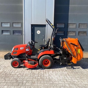 May include: A red and orange compact tractor with a grass catcher attachment. The tractor has black tires and a black seat. The background is a gray industrial building with a door.