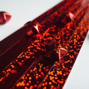 May include: Red iridescent ribbon with a glittery finish. Five red origami stars are scattered around the ribbon.