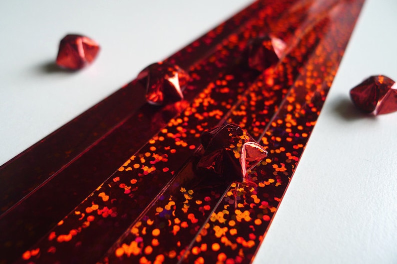May include: Red iridescent ribbon with a glittery finish. Five red origami stars are scattered around the ribbon.