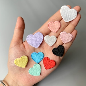 Op de afbeelding: Assortiment van 10 geborduurde vilt hart patches in verschillende kleuren, waaronder roze, paars, blauw, groen, geel, rood, wit en zwart.