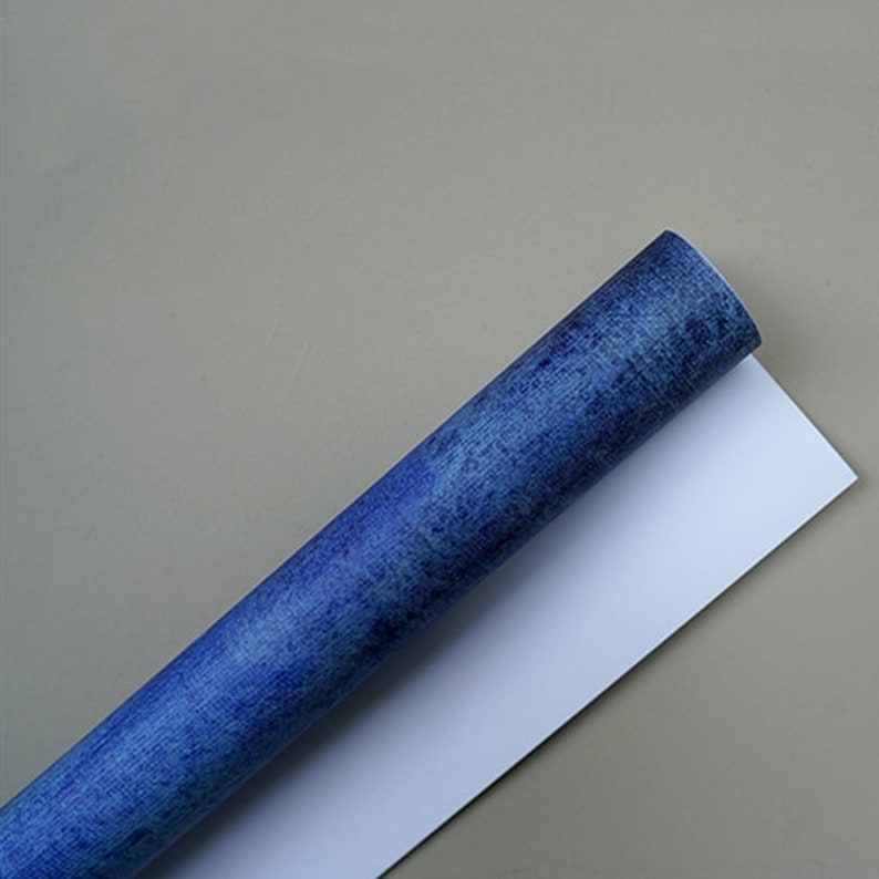 May include: A roll of blue patterned wrapping paper with a white backing. The paper has a textured, distressed look.