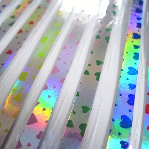 May include: A close-up of a variety of iridescent holographic ribbon with a heart pattern. The ribbon is available in a variety of colors, including blue, green, red, and yellow.