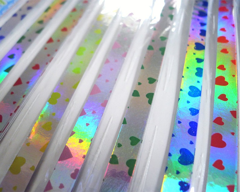 May include: A close-up of a variety of iridescent holographic ribbon with a heart pattern. The ribbon is available in a variety of colors, including blue, green, red, and yellow.