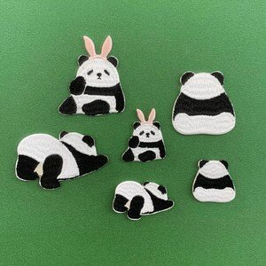 Könnte beinhalten: Sechs schwarze und weiße Bügeleisen-Aufnäher in Form von Pandabären. Die Aufnäher sind in verschiedenen Posen, darunter sitzend, liegend und stehend. Ein Panda trägt rosa Hasenohren.