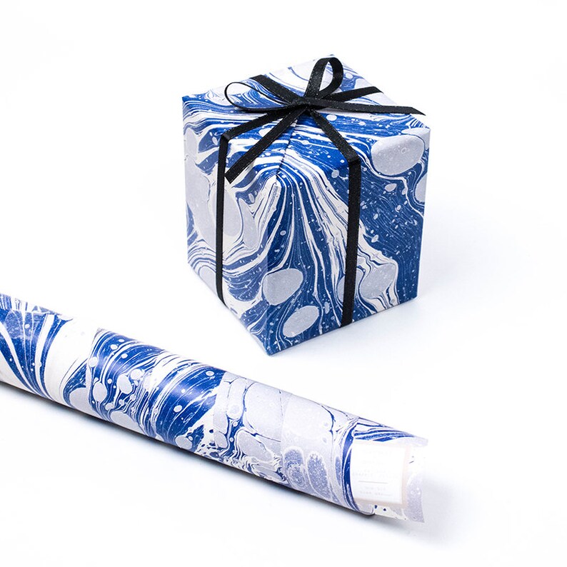 Puede incluir: Un rollo de papel de regalo marmoleado azul y blanco con una caja de regalo envuelta en el mismo papel y atada con una cinta negra.