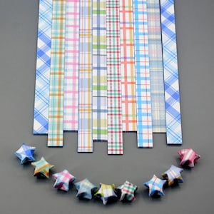 Pode incluir: Conjunto de tiras de papel de origami xadrez de várias cores, dispostas verticalmente, com uma fileira de estrelas de origami feitas com o papel de baixo.