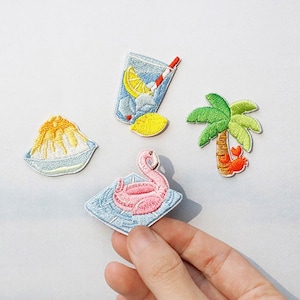 以下が含まれることがあります： 夏をテーマにしたアイロン接着式の刺繍パッチ4枚セット。レモネードグラス、カニの付いたヤシの木、かき氷の入ったボウル、ピンクのフラミンゴフロートの4種類です。