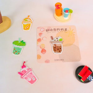 Op de afbeelding: Vier geborduurde strijkpatches met verschillende soorten melkdrankjes. De patches bevinden zich op een witte achtergrond met een kaart waarop "Don't touch my milk tea" in het Chinees en Engels staat.