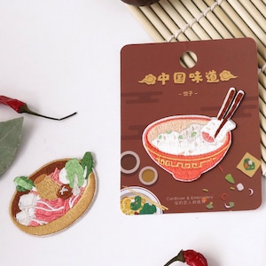 Op de afbeelding: Twee geborduurde strijkpatches met Chinees eten. Eén patch toont een kom rijst met eetstokjes, de andere toont een hotpot met groenten en vlees. De kaart luidt "Chinese smaken - Eén hap".