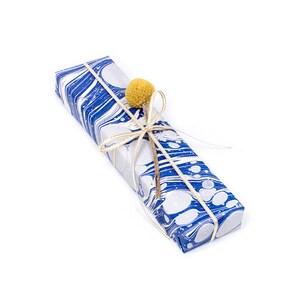 Puede incluir: Una caja de regalo de m&aacute;rmol azul y blanco atada con una cinta dorada y adornada con una peque&ntilde;a flor amarilla.