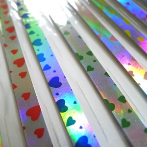 May include: Assortment of iridescent ribbon with heart patterns in red, green, blue, and yellow. The ribbon is packaged on a white card.