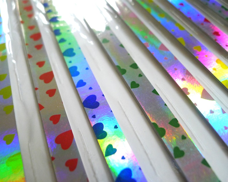 May include: Assortment of iridescent ribbon with heart patterns in red, green, blue, and yellow. The ribbon is packaged on a white card.