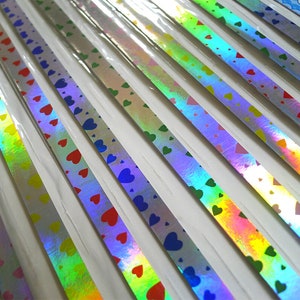 May include: Assortment of iridescent holographic washi tape with a heart pattern in various colors, including pink, blue, green, and red.