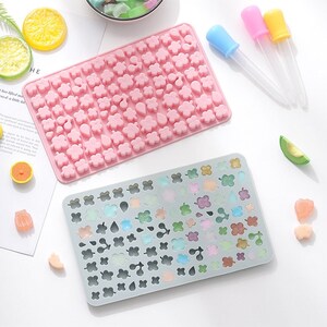 May include: Two silicone moulds for making candy or chocolate. The pink mould has a variety of small shapes, including flowers, hearts, and leaves. The grey mould has the same shapes but is filled with colourful candies.
