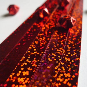 May include: Red iridescent paper strips with a glittery finish. The strips are arranged in a fan shape with red origami stars scattered around them.