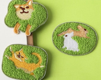 May include: Three embroidered iron-on patches featuring a Shiba Inu dog, a cat, and two rabbits. The patches are on a green background and have a fuzzy texture.