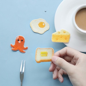 May include: Five embroidered iron-on patches featuring a fried egg, a slice of cheese, a piece of toast with butter, an octopus, and a fork.