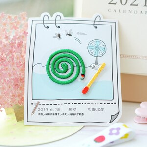 Puede incluir: Una tarjeta blanca con una espiral de mosquito verde y una cerilla amarilla. La tarjeta tiene un dibujo de un ventilador y dos mosquitos. El texto en la tarjeta dice "2019.6.18. 烈 气温40度 半夜被蚊子杂醒了令天,妈妈买了蚊香".