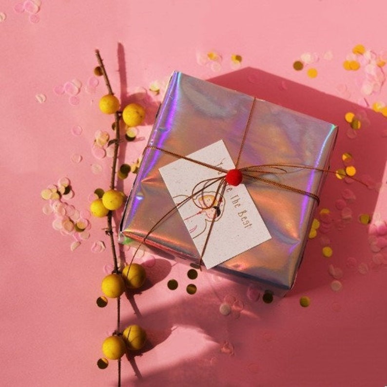 May include: A holographic gift box with a brown ribbon and a red bow. The box has a card attached to it with the text "Be the Best" and a drawing of two people.