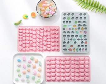 May include: Four pink silicone moulds for making candy or chocolate. The moulds feature different designs, including flowers, animals, and geometric shapes. A bowl of colourful candies is also shown.