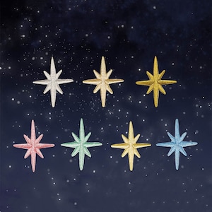 Puede incluir: Ocho parches de estrellas bordadas en varios colores, incluyendo plata, oro, rosa, verde y azul. Cada estrella tiene ocho puntas y está sobre un fondo azul oscuro con motas blancas, que simula un cielo nocturno.
