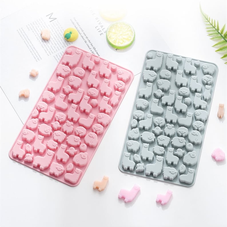 May include: Two silicone moulds for making candy or chocolate. One mould is pink and the other is grey. Both moulds feature a repeating pattern of small llama and pig shapes.