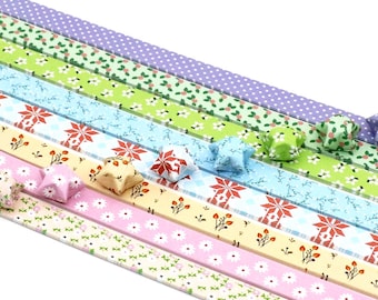 May include: Assortment of colorful origami paper strips with various floral and geometric patterns. The strips are arranged in a rainbow pattern with origami stars made from the paper.
