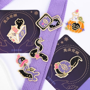 Puede incluir: Un conjunto de seis parches bordados para planchar con diferentes diseños de temática de Halloween, incluyendo un gato negro, una serpiente, una calabaza y un cuervo. Los parches están todos sobre un fondo morado con detalles dorados. El texto "魔法觉醒" es visible en dos de los parches.