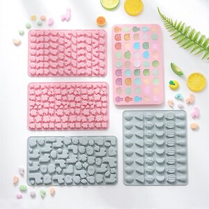 May include: Four silicone candy moulds with different shapes. The moulds are pink and grey and feature various designs, including animals, fruits, and flowers.