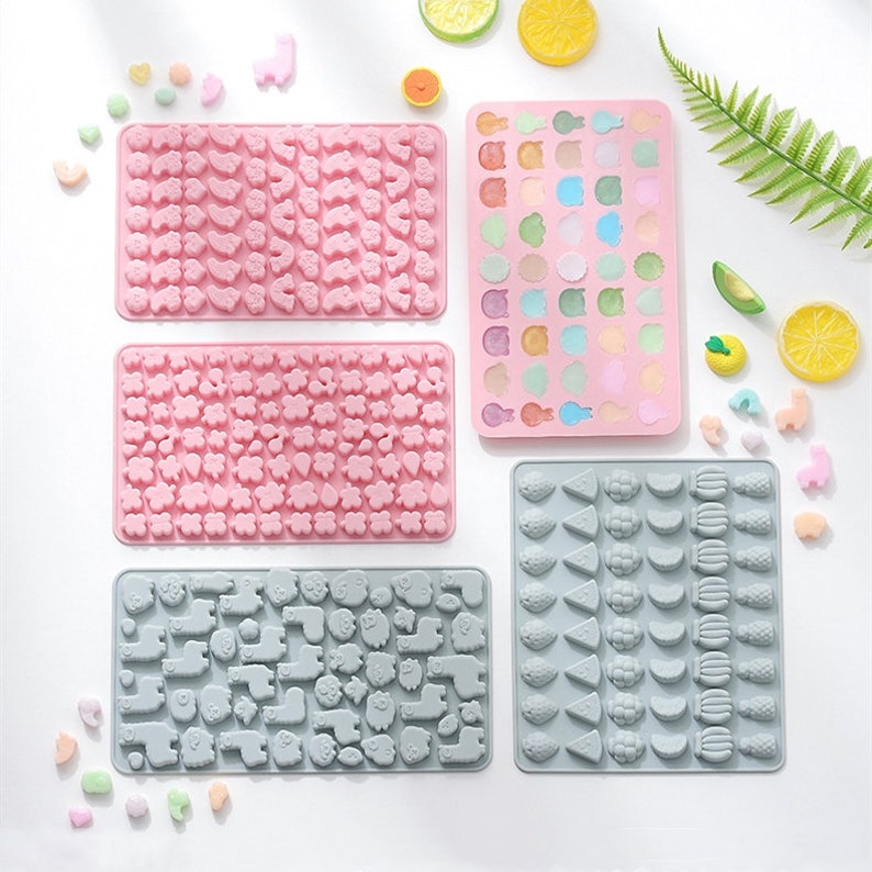 May include: Four silicone candy moulds with different shapes. The moulds are pink and grey and feature various designs, including animals, fruits, and flowers.