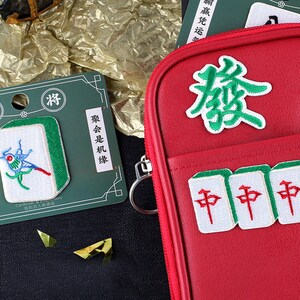 May include: Red zippered pouch with embroidered mahjong tiles and Chinese characters. The pouch has a green and white color scheme. The text on the pouch reads "聚会是机缘" which translates to "Gathering is fate".