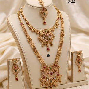 May include: A gold-toned jewelry combo set, including a necklace, earrings, and a headpiece, displayed on a mannequin. The set features intricate floral and geometric designs with red, green, and white accents. The text "Premium Quality Combo Set F-22" is visible.