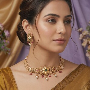 May include: A gold-toned necklace and earring set. The necklace features a central floral design with a green gemstone, surrounded by red and white accents. The earrings mirror the necklace's design, with a pearl drop.
