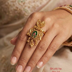 May include: A gold ring with a peacock design, incorporating green and red details. The ring has detailed patterns and small hanging ornaments. The text "SH.viti he. No.24" is visible.