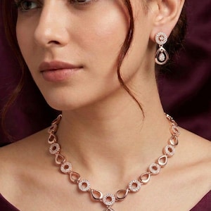 Puede incluir: Conjunto de collar y pendientes en oro rosa, con un colgante en forma de lágrima y detalles circulares adornados con brillantes piedras CZ. Se aprecia el texto "Premium Quality CZ AD Necklace A-14".