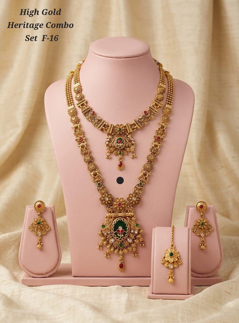 May include: A gold-coloured heritage jewellery set, comprising two necklaces, earrings, and a headpiece, presented on pink stands. The necklaces showcase intricate floral and geometric designs with red, green, and gold accents. The text "High Gold Heritage Combo Set F-16" is visible.