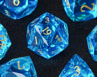 May include: Set of seven blue and gold polyhedral dice. The dice are transparent with gold numbering. The set includes a D4, D6, D8, D10, D12, D20, and a percentile die.