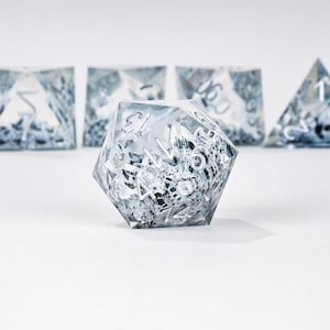 Peut inclure: Un ensemble de d&eacute;s clairs &agrave; plusieurs faces avec un int&eacute;rieur marbr&eacute; noir et blanc. Les d&eacute;s ont des chiffres blancs et sont con&ccedil;us pour les jeux de soci&eacute;t&eacute;. L'image montre un d&eacute; d20 au centre, avec d'autres d&eacute;s en arri&egrave;re-plan.