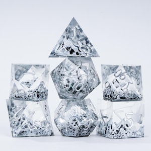 Peut inclure: Un ensemble de sept d&eacute;s poly&eacute;driques de diff&eacute;rentes formes, dont un d4, d6, d8, d10, d12, d20 et un d&eacute; de pourcentage. Les d&eacute;s sont transparents avec un effet marbr&eacute; argent&eacute; et noir et des chiffres argent&eacute;s.