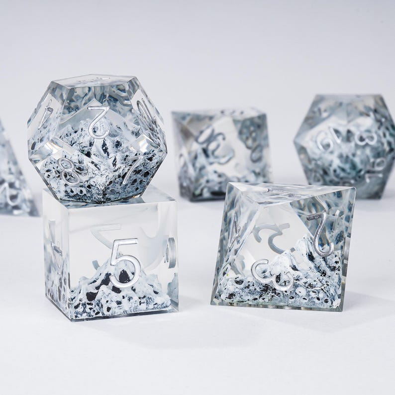 Peut inclure: Ensemble de d&eacute;s transparents &agrave; multiples faces, avec des chiffres argent&eacute;s et un int&eacute;rieur textur&eacute; et neigeux. Ces d&eacute;s, con&ccedil;us pour les jeux de soci&eacute;t&eacute;, sont pr&eacute;sent&eacute;s sur une surface blanche. L'ensemble comprend diff&eacute;rentes formes, comme un cube et un d&eacute; &agrave; 20 faces.