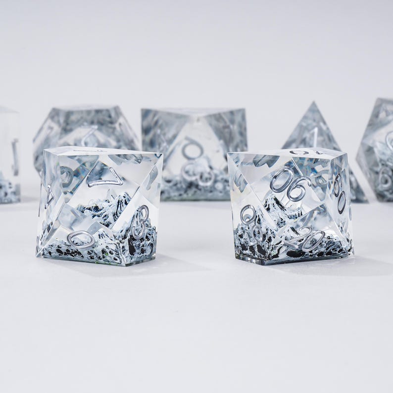 Peut inclure: Un ensemble de d&eacute;s transparents &agrave; multiples faces, avec des chiffres argent&eacute;s et un int&eacute;rieur sombre et textur&eacute;. Les d&eacute;s sont dispos&eacute;s sur une surface blanche, mettant en valeur leurs formes g&eacute;om&eacute;triques et leurs d&eacute;tails complexes. Pour les jeux de soci&eacute;t&eacute;.